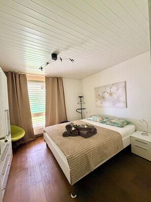 A bedroom with a bed, a bedside table, a lamp, a window with curtains, and a radiator. - Bijou makes your vacation magical. (Diemtigen)