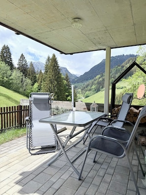 En udendørs terrasse med et bord og stole, et træhegn og udsigt til bjerge.
