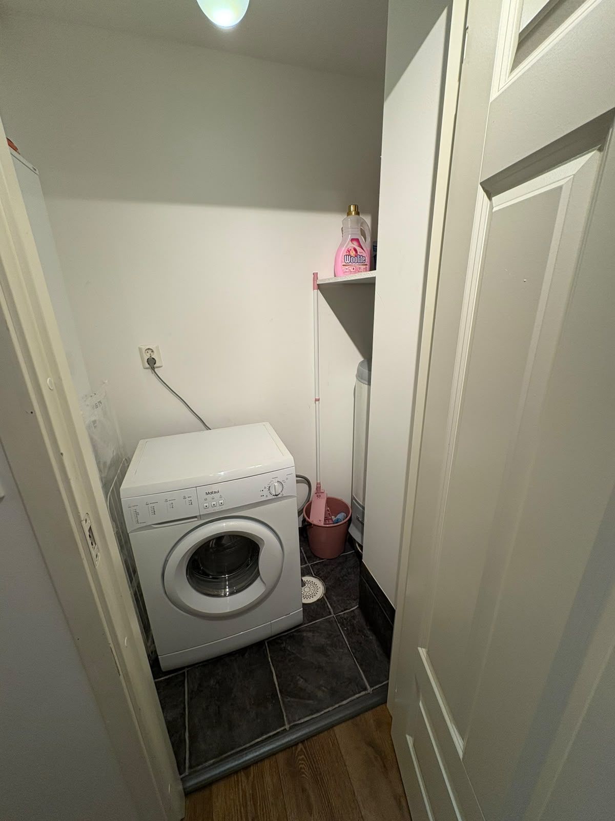 Ein kleiner Hauswirtschaftsraum mit einer Waschmaschine mit Frontlader, einem Mop und einer kleinen Ablagefläche.