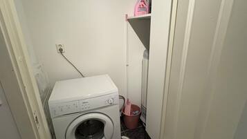 Ein kleiner Hauswirtschaftsraum mit einer Waschmaschine mit Frontlader, einem Mop und einer kleinen Ablagefläche.