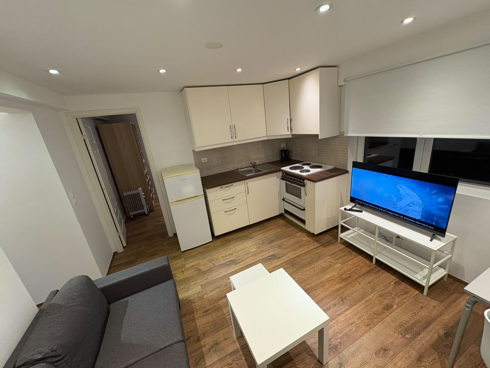 A compact living space with a kitchenette, a flat-screen TV, a sofa, and a small table.