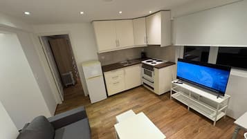 A compact living space with a kitchenette, a flat-screen TV, a sofa, and a small table.