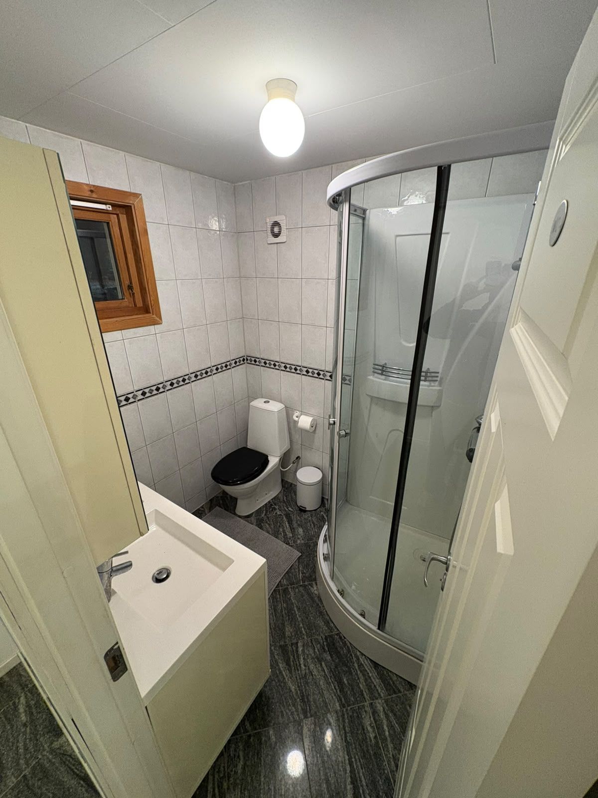 Un baño pequeño con un lavamanos blanco, un inodoro y una ducha con mampara de vidrio.