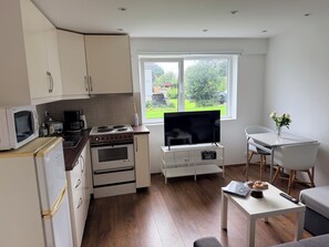 A compact kitchen with a stove, microwave, and refrigerator. There's a dining area with a table and chairs, and a window with a view of greenery.