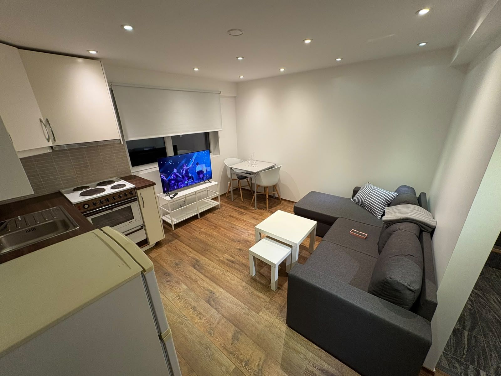 A modern living room with a flat-screen TV, a dining area, and a kitchen with a stove and sink.