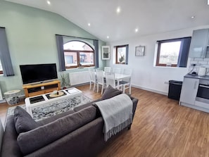 En moderne stue med sofa, fjernsyn, spisebord og et tekøkken.