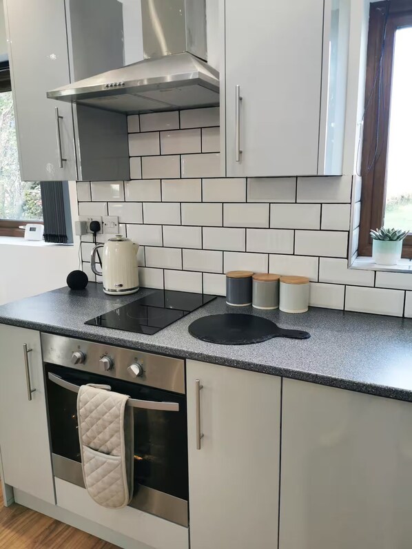 A modern kitchen with white cabinets, a stainless steel range hood, a black induction cooktop, and a built-in oven.