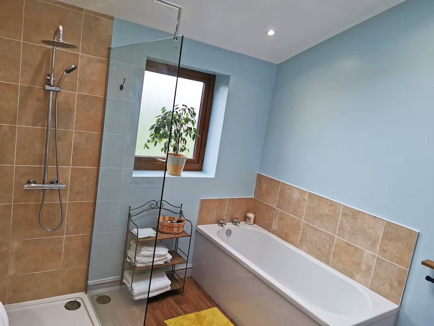A bathroom with a bathtub, a shower, a window with a plant, and a shelf with towels.