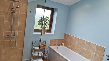 A bathroom with a bathtub, a shower, a window with a plant, and a shelf with towels.