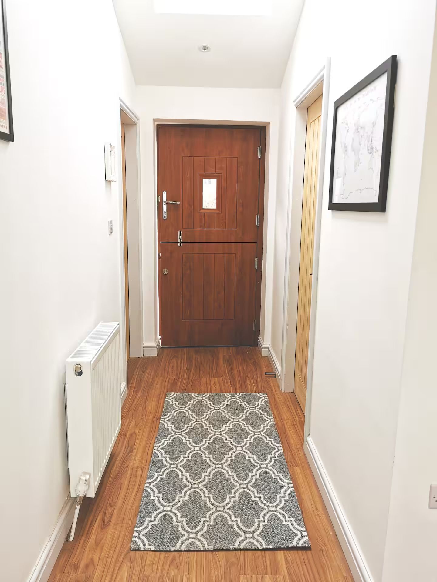 A hallway with a wooden door, a radiator, a patterned rug, and a framed picture on the wall.