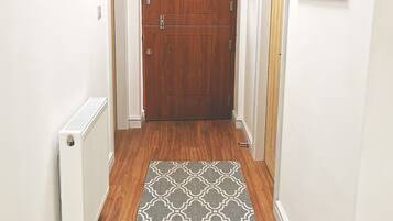 A hallway with a wooden door, a radiator, a patterned rug, and a framed picture on the wall.