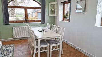 En matplats med ett vitt bord och stolar, ett element, ett fönster med gardiner och en liten växt på fönsterbrädan.
