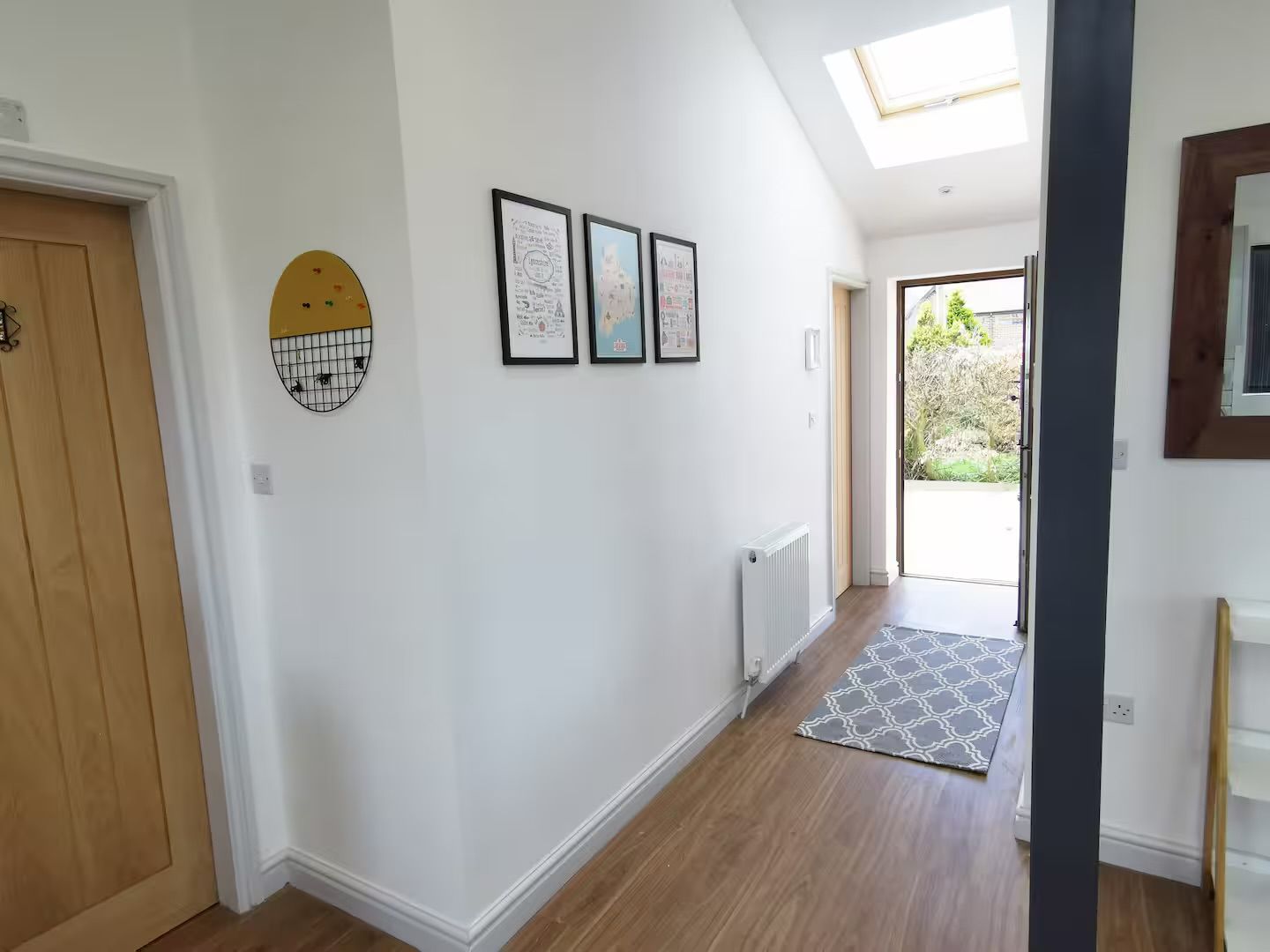 Un pasillo con puerta de madera, un radiador y un tapete estampado que conduce a una puerta con vistas al exterior.