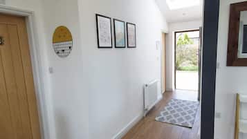 Un pasillo con puerta de madera, un radiador y un tapete estampado que conduce a una puerta con vistas al exterior.