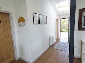A hallway with a wooden door, a radiator, and a patterned rug leading to a door with a view of greenery outside.