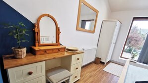 Ein Schlafzimmer mit einem Holzkasten, einem Spiegel, einem Fenster und Blick ins Freie.