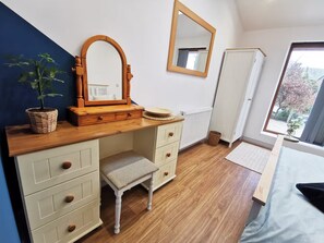 Ein Schlafzimmer mit einem Holzkasten, einem Spiegel, einem Fenster und Blick ins Freie.