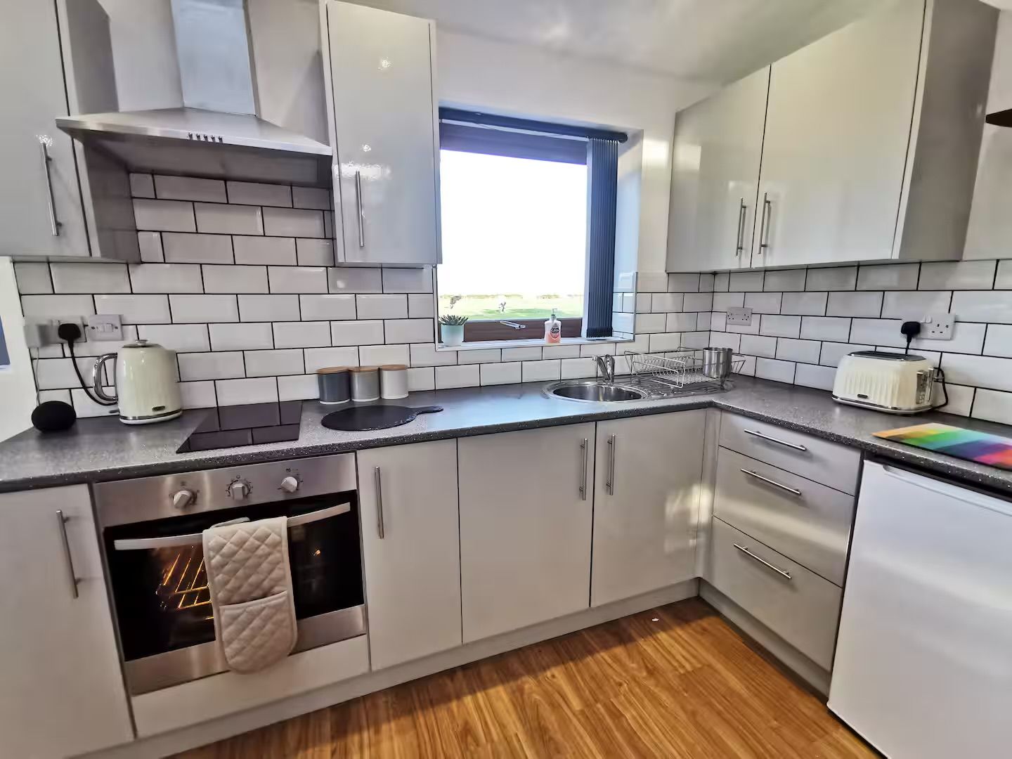 A modern kitchen with white cabinets, a built-in oven, a window, and a toaster.