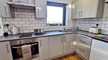 A modern kitchen with white cabinets, a built-in oven, a window, and a toaster.