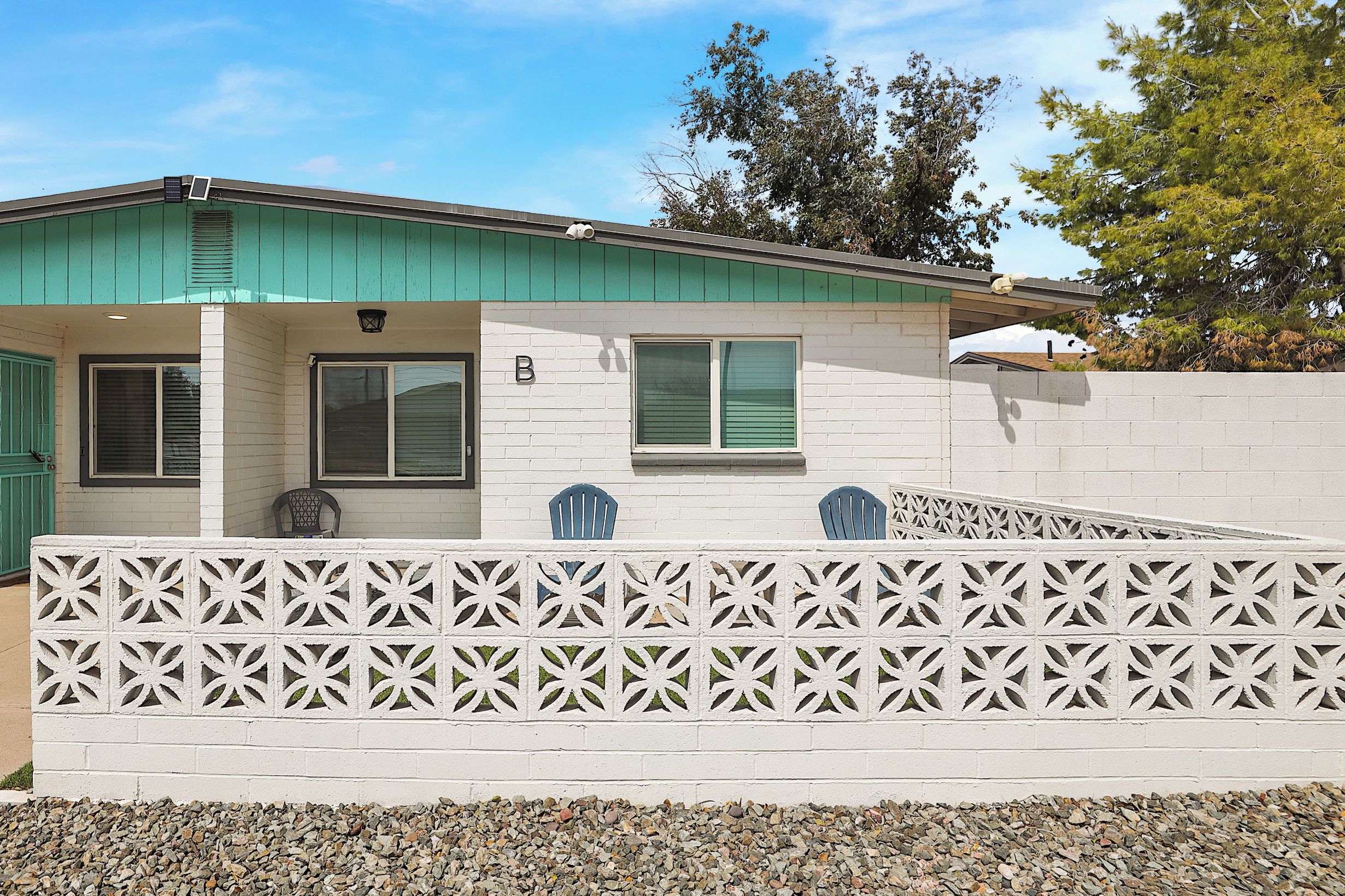 A single-story house with a green roof, white exterior walls, and a white fence with a geometric pattern.