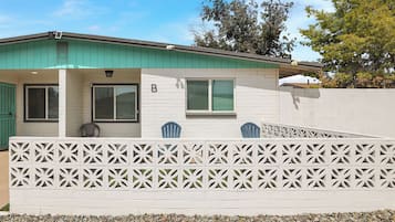 A single-story house with a green roof, white exterior walls, and a white fence with a geometric pattern.