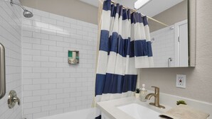 Un bagno con una vasca da bagno bianca, un lavabo con rubinetto dorato, una tenda da doccia azzurro e bianco a righe e una parete rivestita di piastrelle bianche.