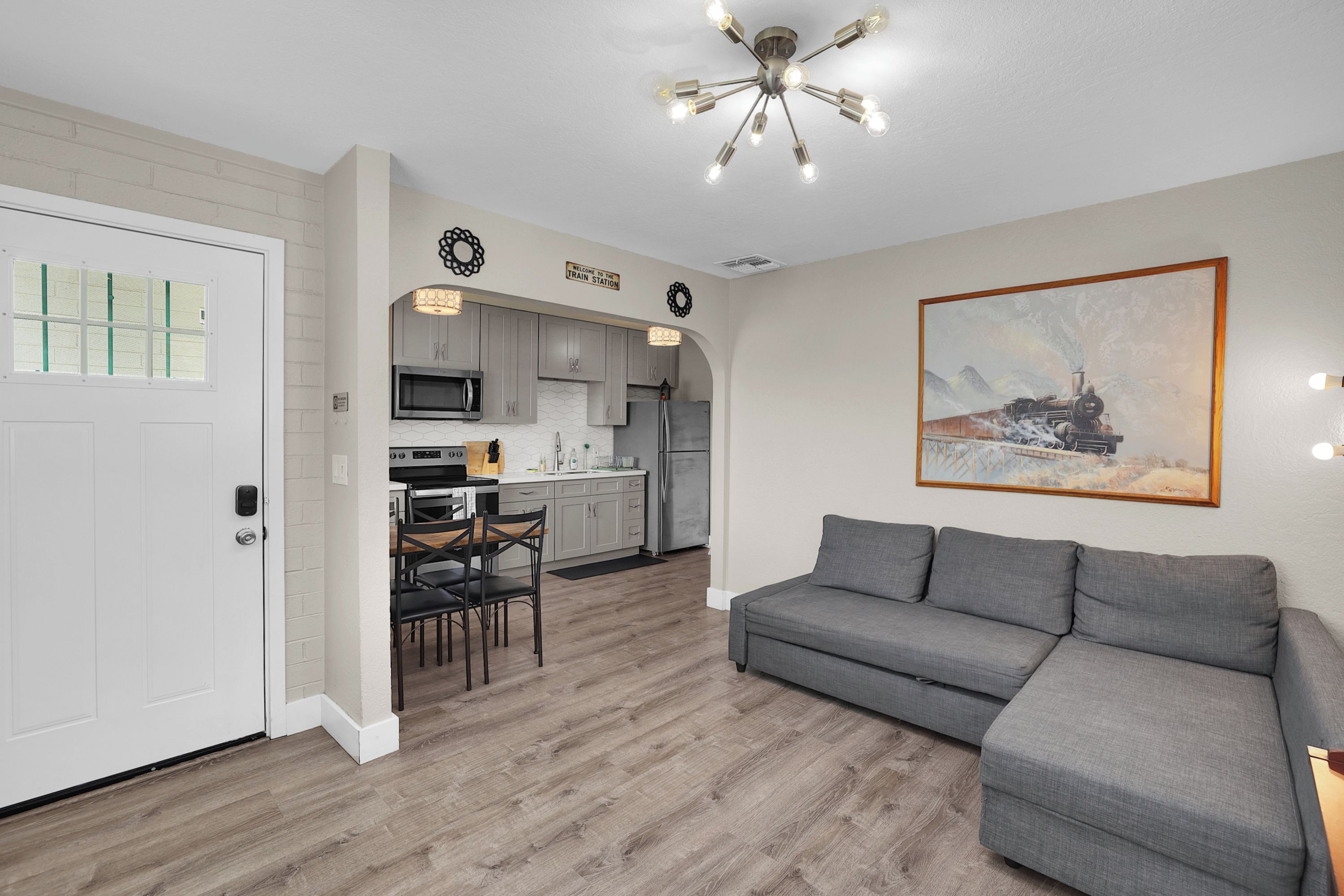 A modern kitchen with a dining area, a gray sofa, and a painting of a train on the wall.
