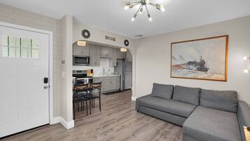 A modern kitchen with a dining area, a gray sofa, and a painting of a train on the wall.