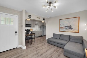 A modern kitchen with a dining area, a gray sofa, and a painting of a train on the wall.