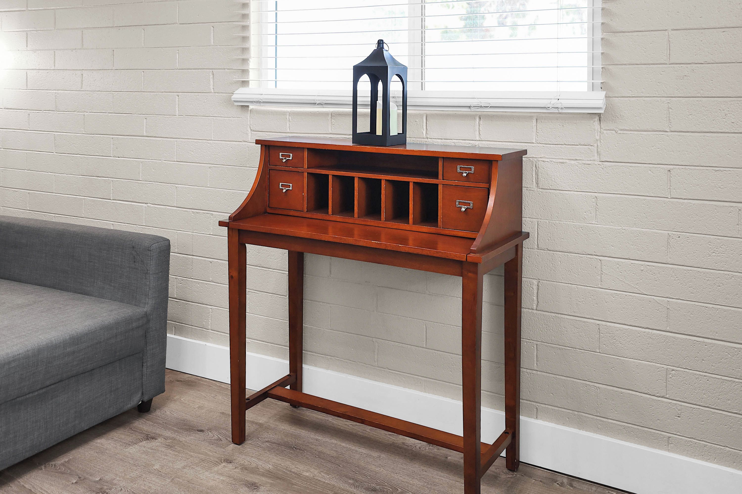 A wooden side table with drawers against a white brick wall, positioned next to a grey sofa.