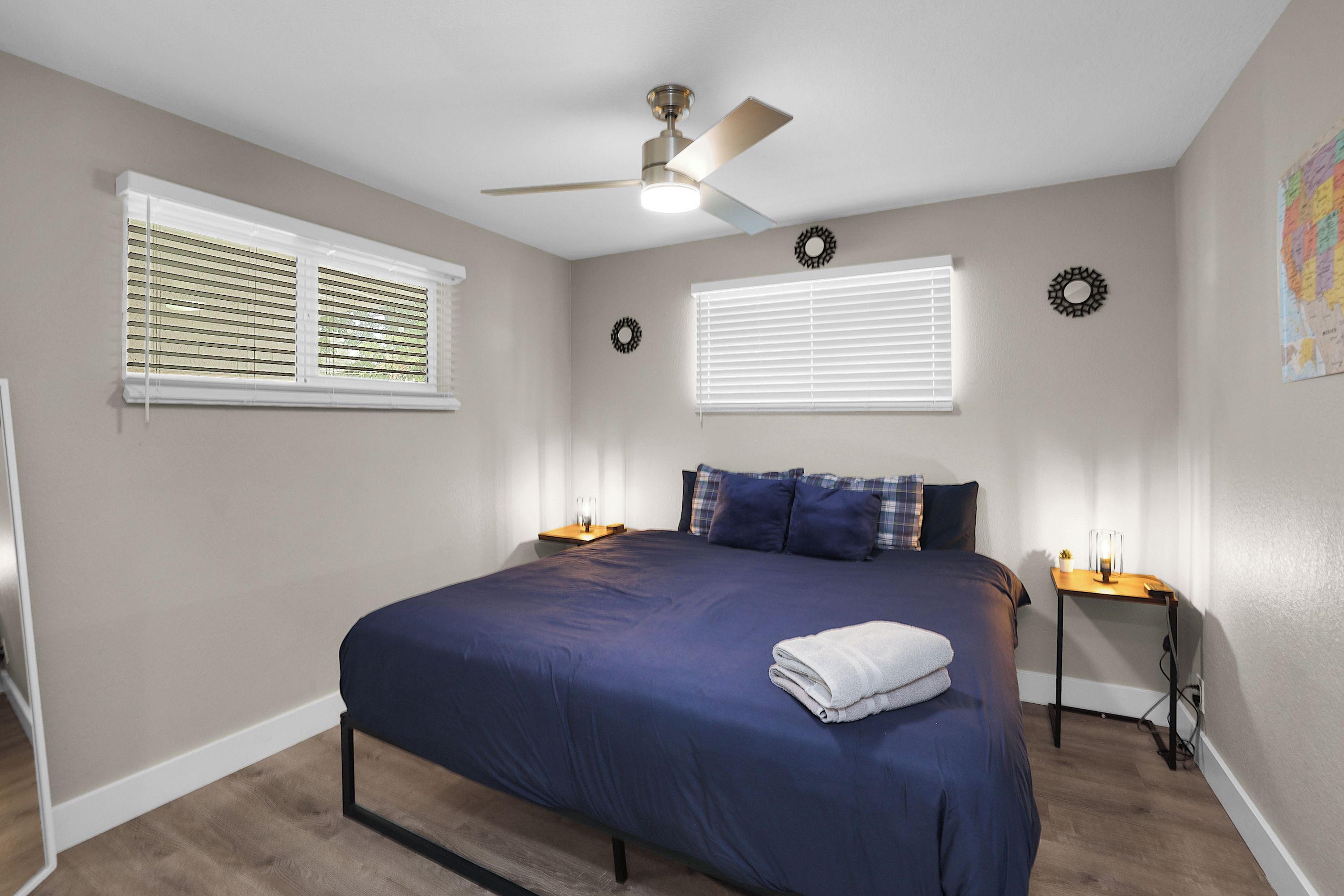 A bedroom with a bed, a ceiling fan, two bedside tables, and a window with blinds.