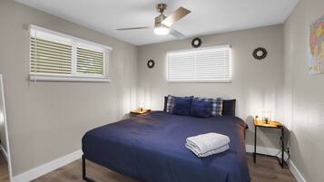 A bedroom with a bed, a ceiling fan, two bedside tables, and a window with blinds.