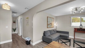Un soggiorno moderno con un divano angolare grigio, un tavolo da pranzo in legno e un angolo cottura con rivestimento in mattoni.