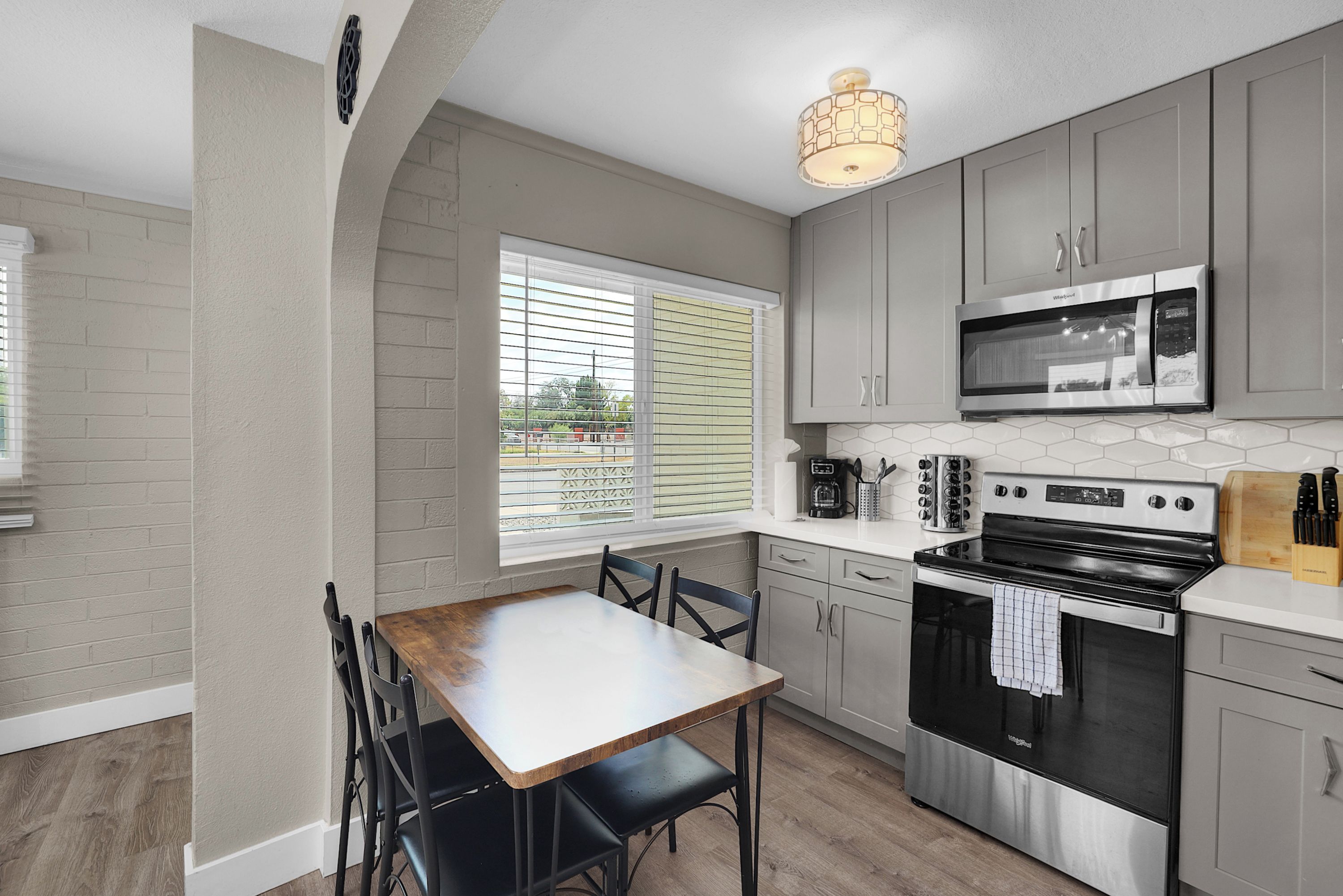 A kitchen with a dining table, chairs, a microwave, a stove, and a window with blinds.