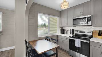 A kitchen with a dining table, chairs, a microwave, a stove, and a window with blinds.