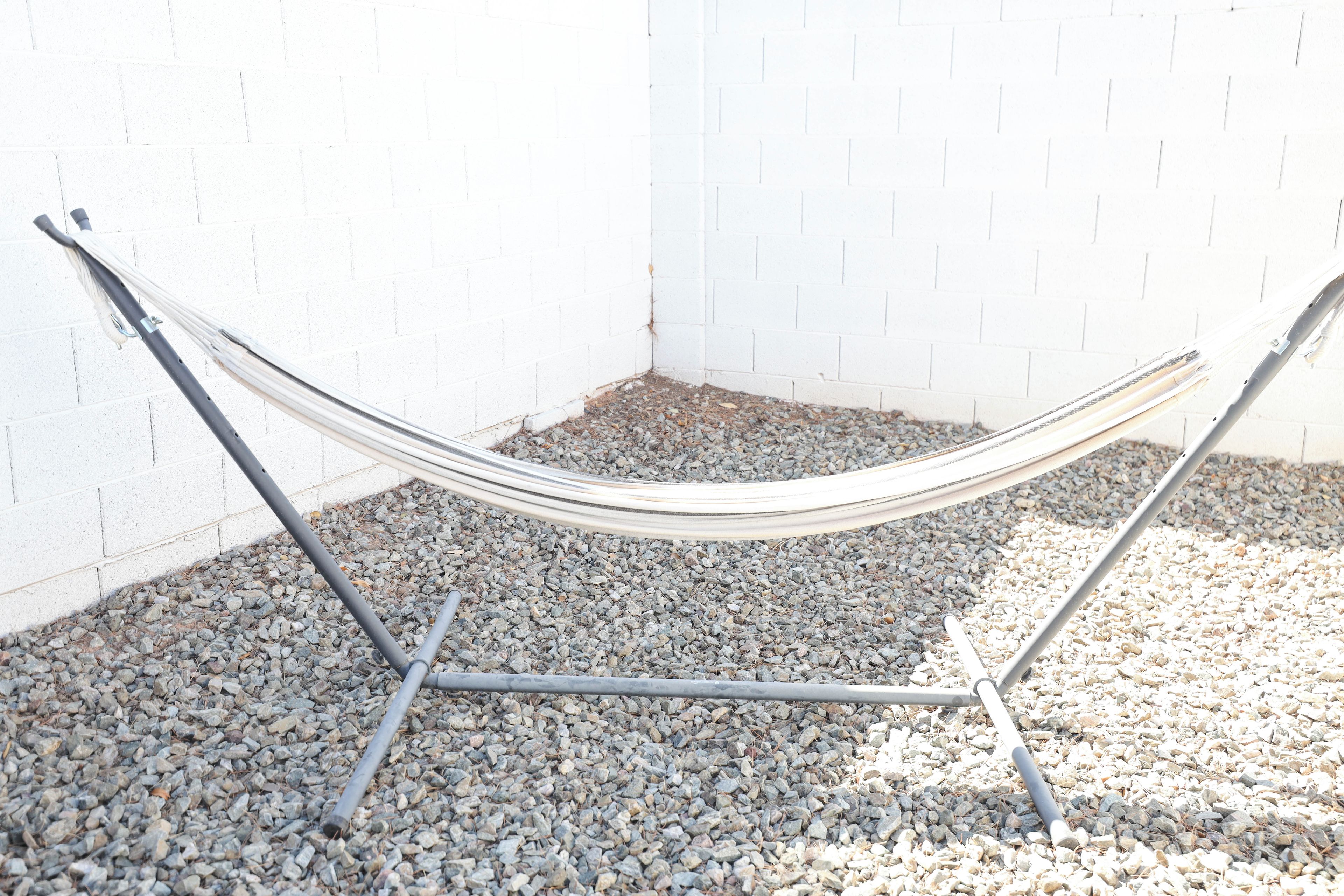 A hammock set up against a white brick wall on a gravel surface.