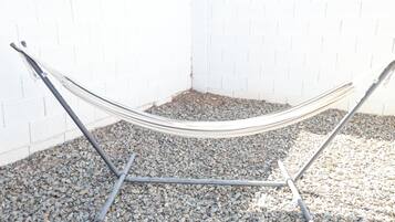 A hammock set up against a white brick wall on a gravel surface.