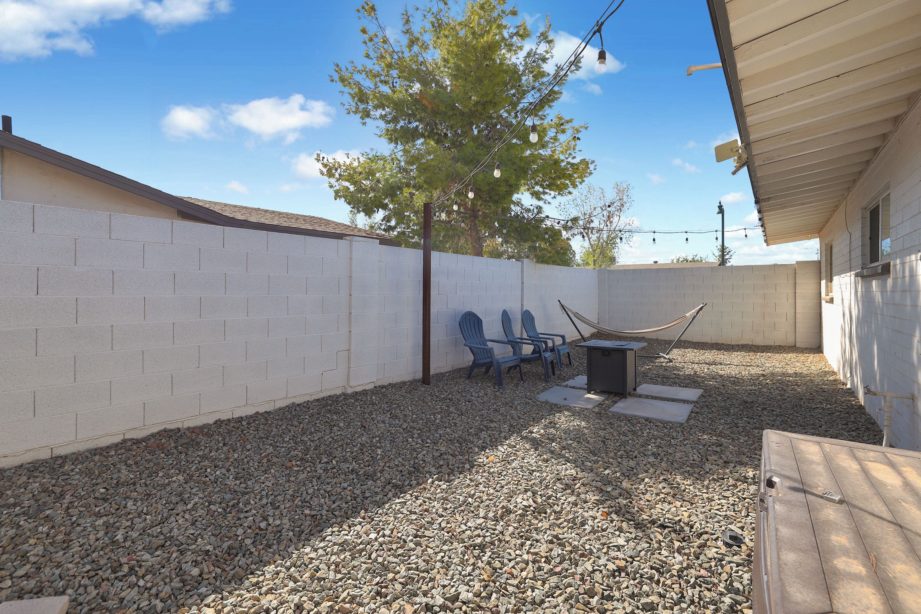 A backyard with a white brick wall, a tree, and a hammock.