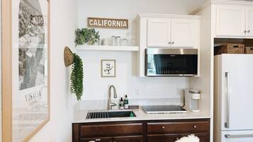 A kitchen with white cabinets, a stainless steel refrigerator, a microwave, and a sink with a faucet.