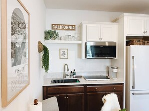 Una cocina con gabinetes blancos, un refrigerador de acero inoxidable, un microondas y un lavamanos con grifo.