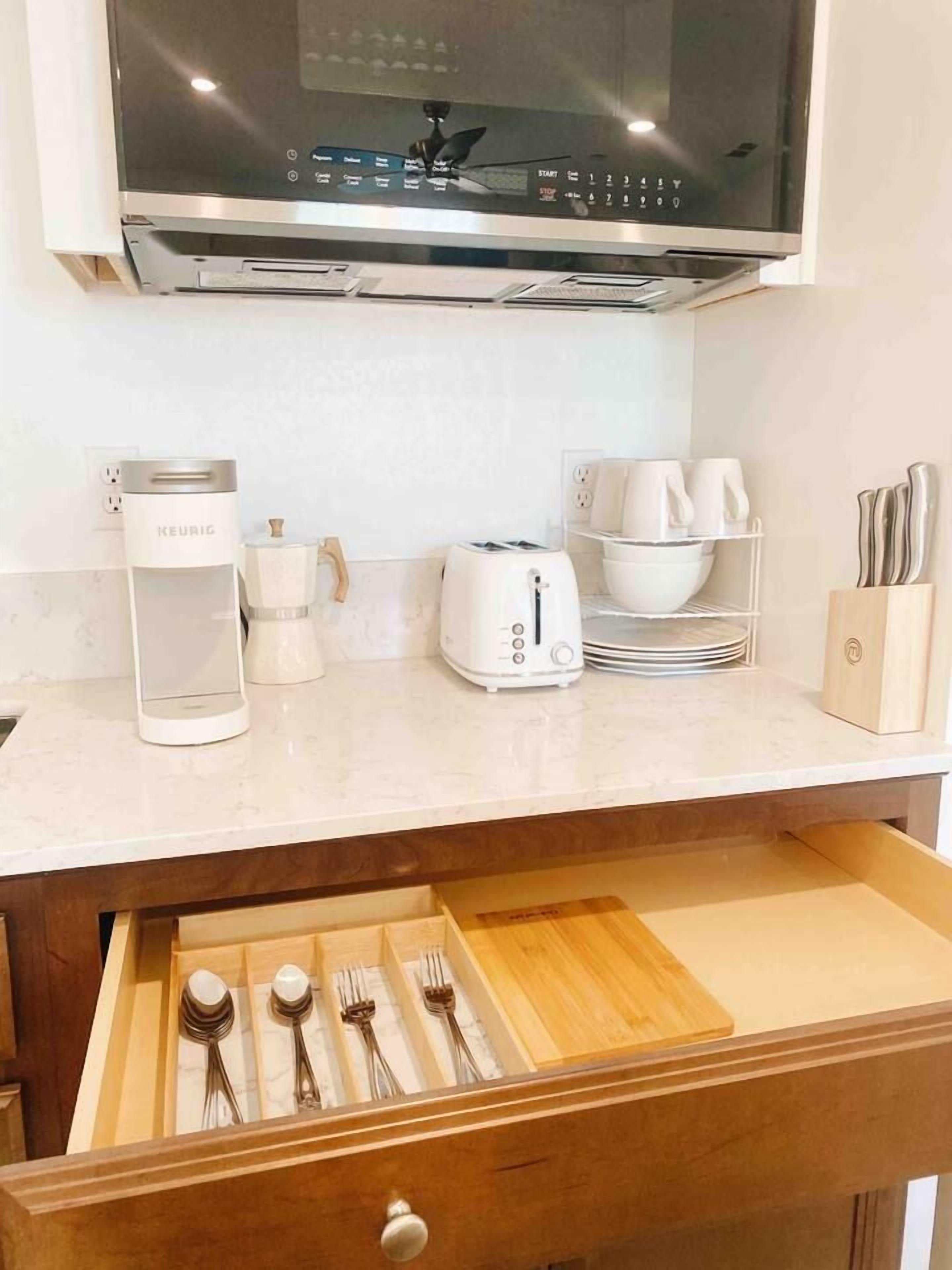 Una cocina con microondas, cafetera, tostadora y un cajón con utensilios.