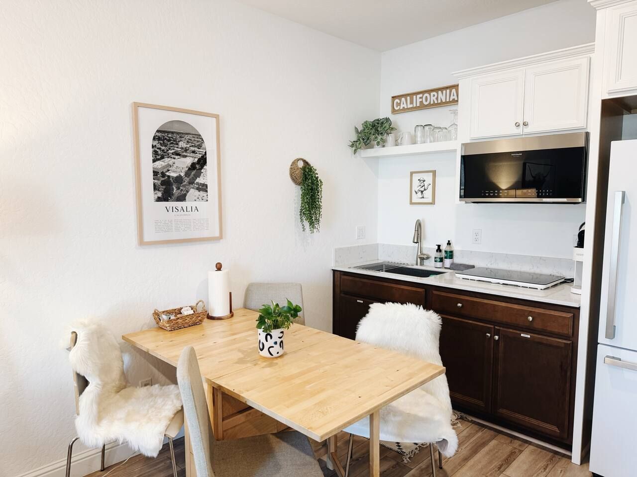 Une cuisine moderne avec une table en bois, des chaises blanches, un four à micro-ondes en acier inoxydable et un réfrigérateur blanc.