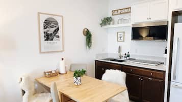 Une cuisine moderne avec une table en bois, des chaises blanches, un four à micro-ondes en acier inoxydable et un réfrigérateur blanc.