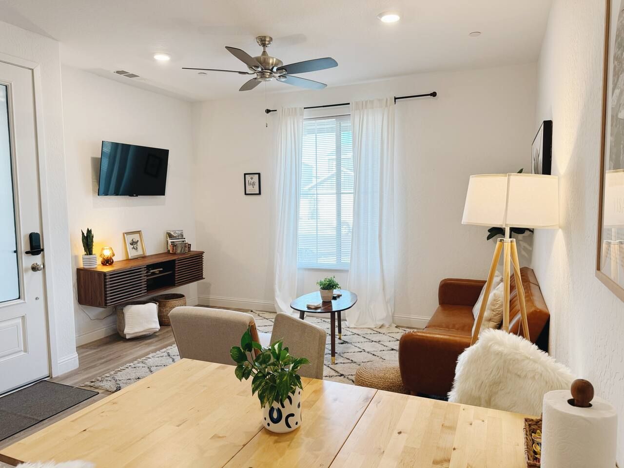 Una sala de estar moderna con una mesa de comedor de madera, un sofá, un televisor montado en la pared y un ventilador de techo.