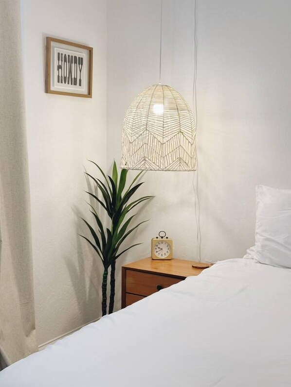 A bedroom with a bed, a bedside table with a clock, a wall-mounted light fixture, and a framed word on the wall.