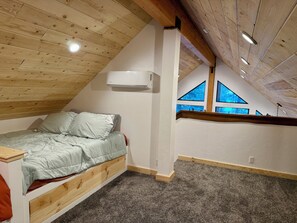 A bedroom with a sloped ceiling, a bed with a wooden headboard, a window with a view, and an air conditioning unit. - Adorable 2-bedroom cabin with filter lake views in charming Cascade (Cascade)