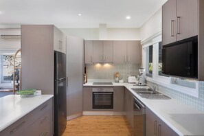 A modern kitchen with a built-in oven, a microwave, and a large window. - Sunbound charming three-bedroom beach house (Pambula Beach)