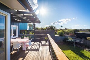 A wooden deck with a table and chairs, a fenced yard, and a clear sky. - Sunbound charming three-bedroom beach house (Pambula Beach)