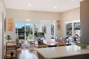 A spacious living area with a dining table, chairs, and a view of the outdoors. - Sunbound charming three-bedroom beach house (Pambula Beach)