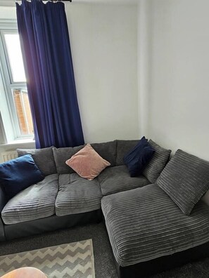 A corner seating area with a sofa and cushions, a window with curtains, and a rug on the floor. - The Cozy Gateshead Escape (Tyne and Wear)